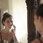 woman night skincare routine applying face cream bedroom mirror