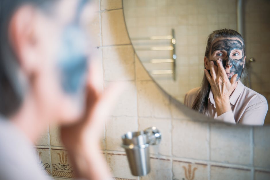 Gommage avant l'été : le rituel complet visage, corps, pieds et cuir chevelu woman applying face scrub in bathroom mirror spring skincare routine