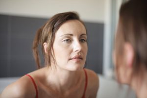 Pourquoi votre visage se fatigue au fil de la journée (et comment y remédier) woman looking in mirror morning versus evening skin fatigue beauty landscape