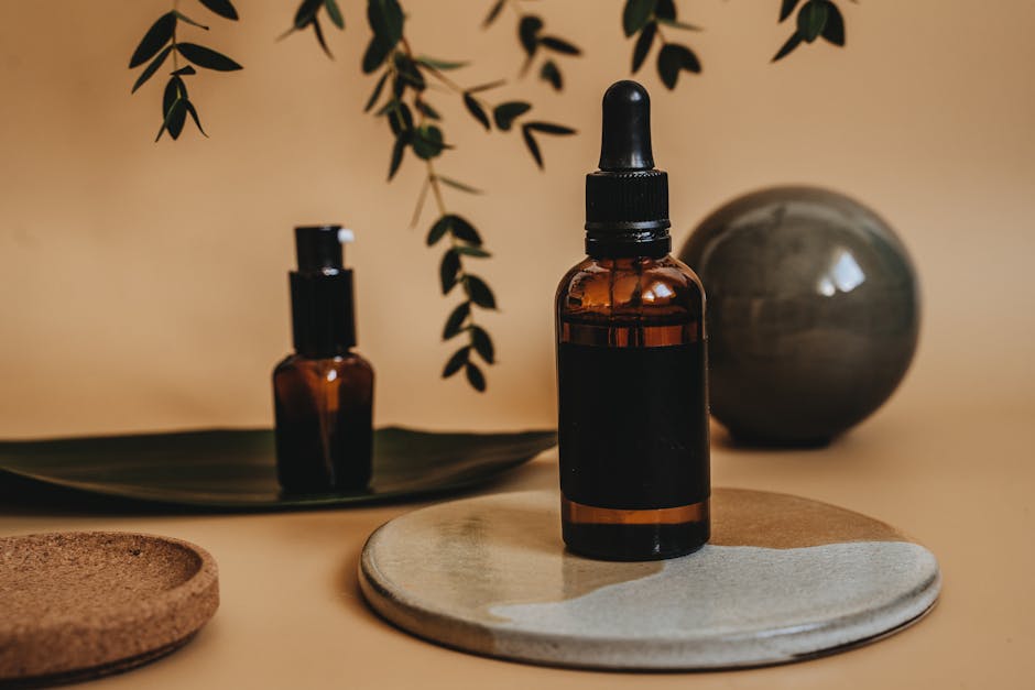dropper bottle with golden facial oil next to green leaves on marble surface