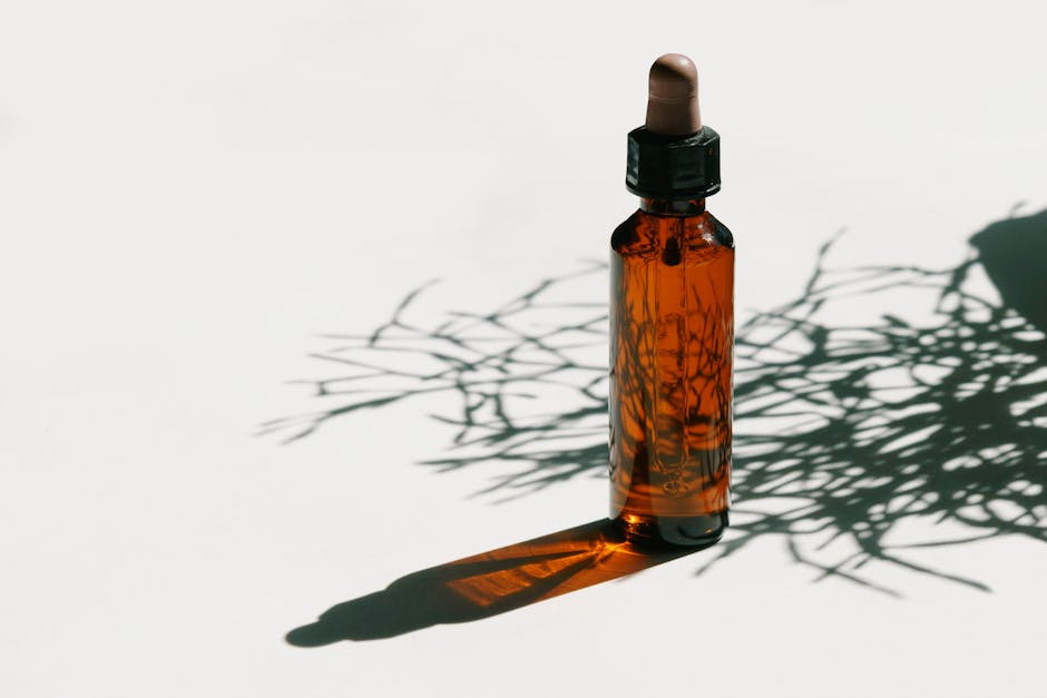 Huile de nuit pour le visage : bienfaits, choix et mode d'emploi glass dropper bottle with plant oil next to green leaves