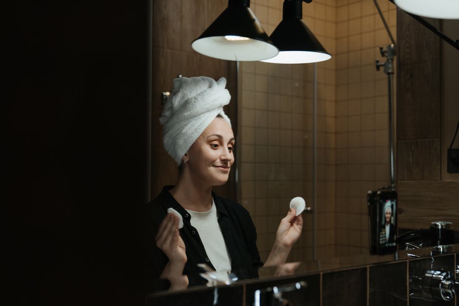 Démaquillage : les erreurs courantes qui abîment votre peau (et comment les éviter) woman removing makeup gently with cotton pad in bathroom mirror evening routine