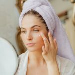 woman applying daily face cream sunscreen morning skincare routine bright natural light