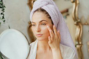 woman applying daily face cream sunscreen morning skincare routine bright natural light