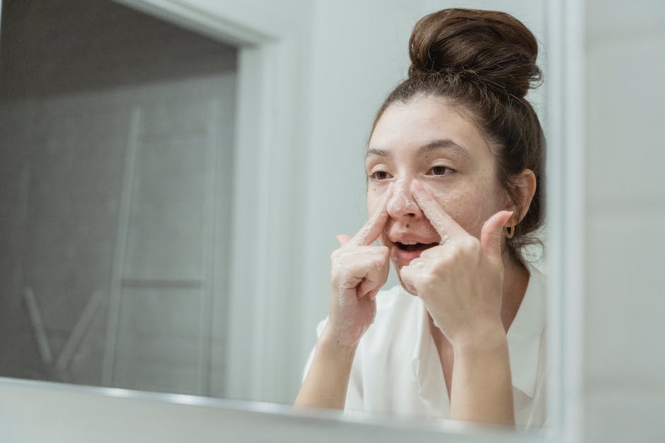Peeling maison : 5 gestes pour retrouver un teint lumineux woman applying exfoliating cleanser face bathroom mirror morning skincare