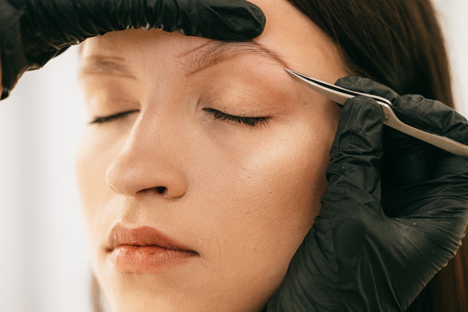 woman plucking eyebrows with tweezers close up beauty routine